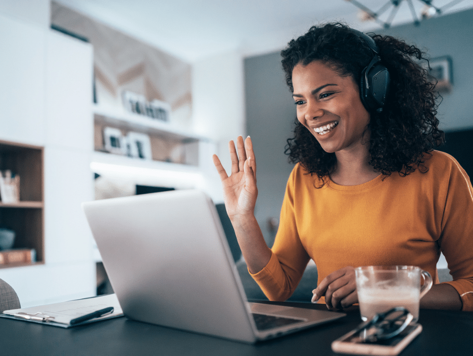 A woman with headphones smiles while using a laptop, indicating enjoyment and engagement with her work or entertainment.