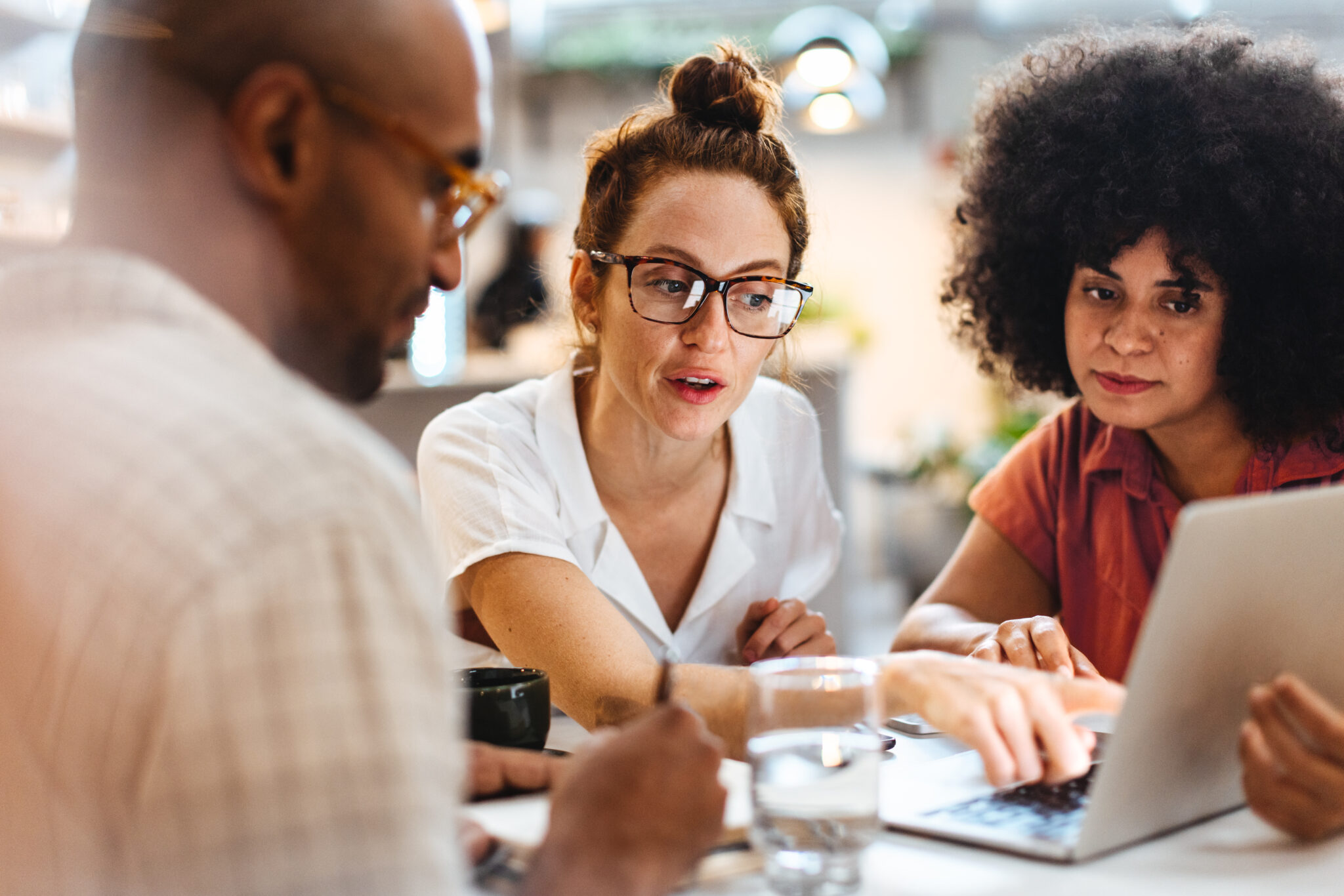 A group of three people focused on a laptop, engaged in conversation about what they see on the screen.