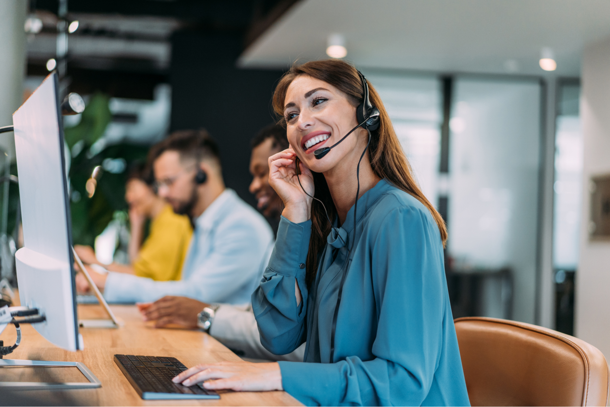 A woman wearing a headset, focused on her computer, working as a call center agent in a modern office environment.