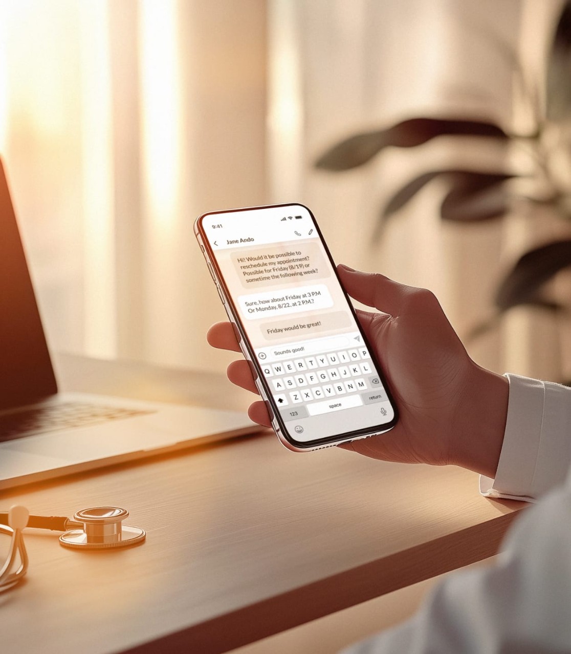Doctor holding smartphone with text messages coordinating an appointment, desk and stethoscope in background