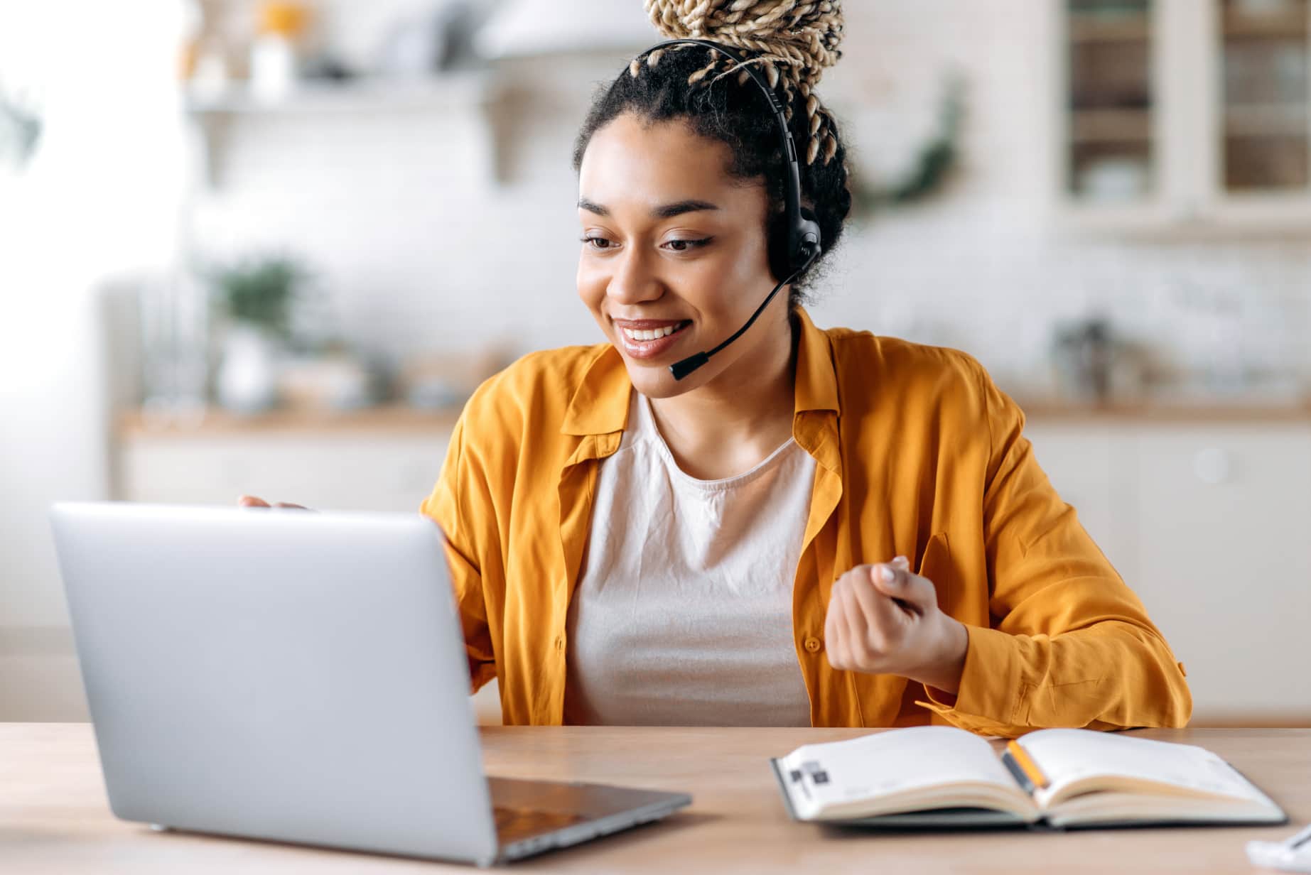 A woman with a headset is at her desk, using a laptop, suggesting she is participating in a remote work or call.